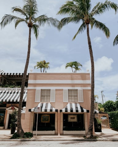 Pink Palm Beach storefront with black and white awnings and palm trees
