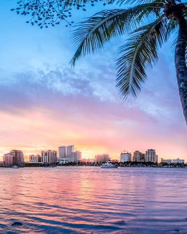 West Palm Beach skyline at sunset reflected on the water with palm trees