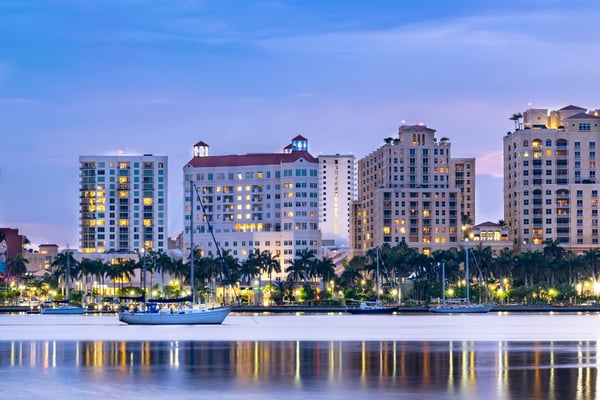 West Palm Beach skyline at dusk reflected on calm water with sailboats and palm trees