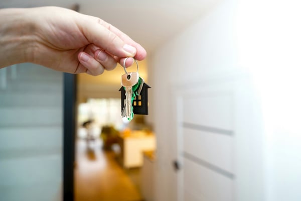 Hand holding house keys in a bright home interior hallway