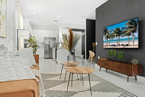 Bright modern living room with open kitchen, palm tree artwork on TV, and tropical decor